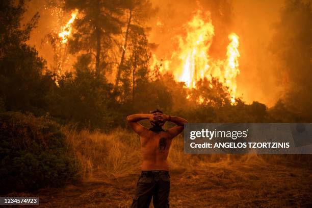 Local resident reacts as he observes a large blaze during an attempt to extinguish forest fires approaching the village of Pefki on Evia island,...