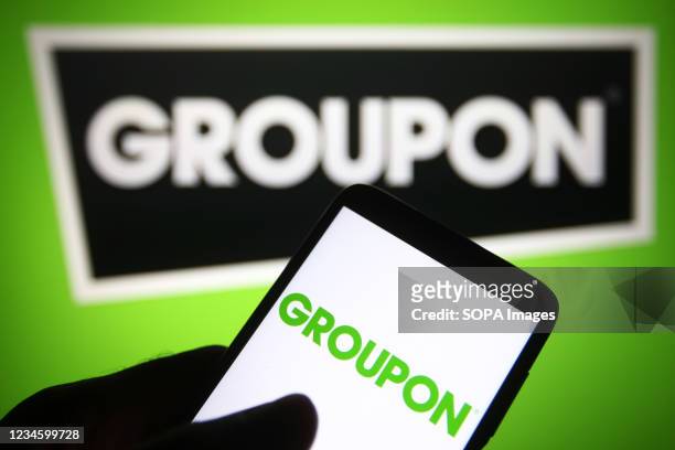 In this photo illustration a Groupon logo is seen on a smartphone and a pc screen.