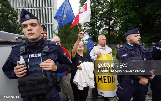 Protester standing between police holds up European and Polish flags to demonstrate in defence of media freedom in Warsaw on August 10, 2021. - A...