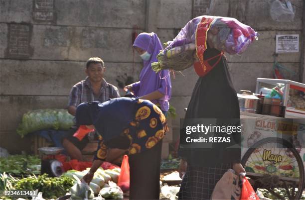 Woman carries a bag of produce at a market in Bekasi on August 11 as Indonesia tries to implement a more restrictive form of lockdown.