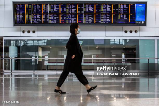 Women walks past a flight information board at Hong Kong International Airport on August 11, 2021.