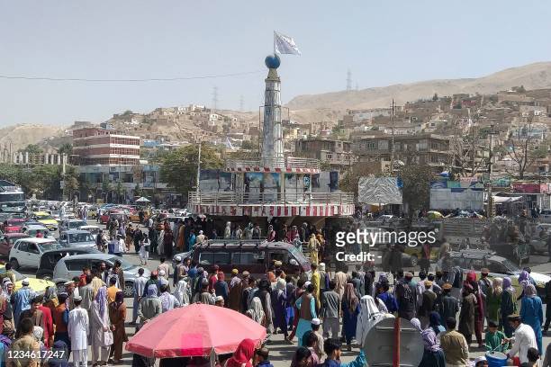 Taliban flag is seen on a plinth with people gathered around the main city square at Pul-e-Khumri on August 11, 2021 after Taliban captured...