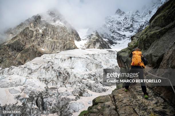 An alpinist holds a fixed rope and walks near the Boccalatte Hut close to the Planpincieux Glacier in Courmayeur, Alps Region, north-western Italy,...