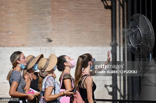Group of woman cool off in front of a cooling fan during a heatwave as they queue at the enterance of the Colosseum in Rome on August 12, 2021. An...