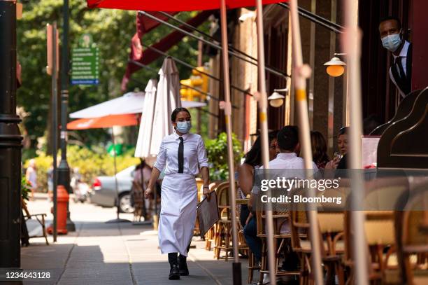 Server wearing a protective mask carries menus in the outdoor dining section of a restaurant in Philadelphia, Pennsylvania, U.S., on Thursday, Aug....