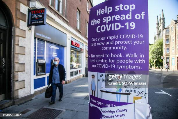 Man wearing a face mask walks past 'Help stop the spread of COVID-19' advert displayed in Edinburgh, Scotland.