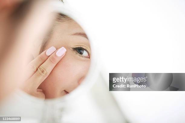young woman looking at self in mirror,skin care - 鏡　女性 ストックフォトと画像