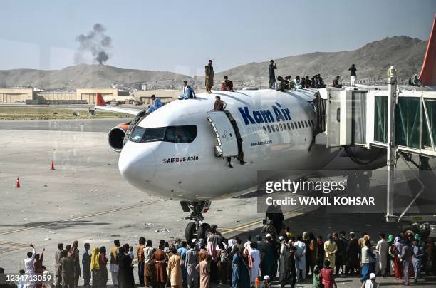 Afghan people climb atop a plane as they wait at the Kabul airport in Kabul on August 16 after a stunningly swift end to Afghanistan's 20-year war,...