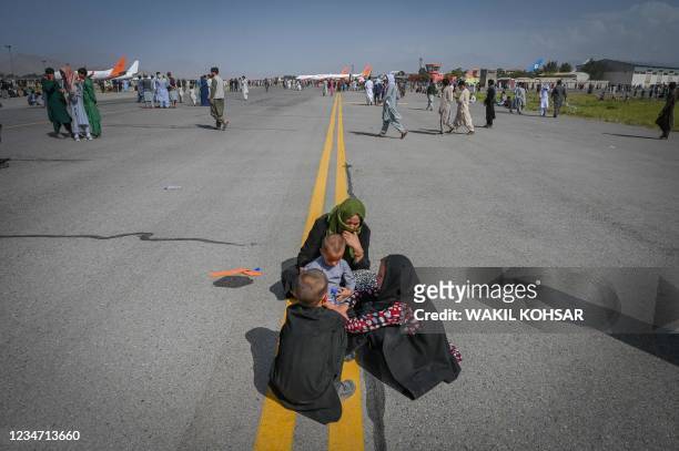 Afghan people sit along the tarmac as they wait to leave the Kabul airport in Kabul on August 16 after a stunningly swift end to Afghanistan's...