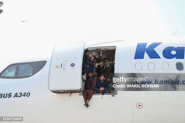 Afghan people climb up on a plane and sit by the door as they wait at the Kabul airport in Kabul on August 16 after a stunningly swift end to...
