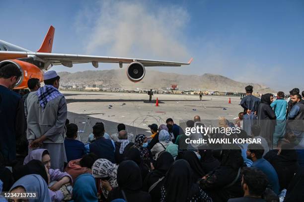 Afghan people sit as they wait to leave the Kabul airport in Kabul on August 16 after a stunningly swift end to Afghanistan's 20-year war, as...