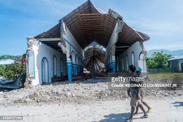 Two Haitians walk past a church destroyed during an earthquake in Les Anglais on August 14, 2021. - At least 1,297 people were killed in the...