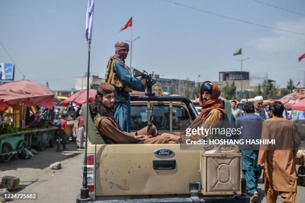 Taliban fighters on a pick-up truck move around a market area, flocked with local Afghan people at the Kote Sangi area of Kabul on August 17 after...