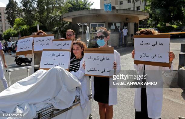 Pharmacist sits on a stretcher holding a sign reading in Arabic "no gasoline = no ambulance" while others stand by holding signs reading "no...