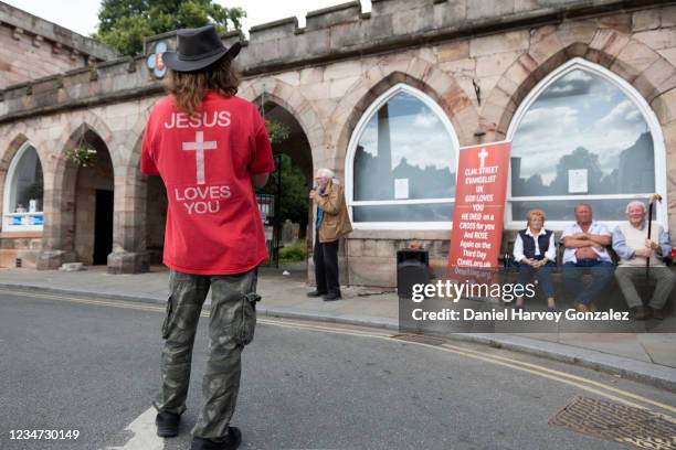 Man wearing a t-shirt that reads "Jesus Loves You" watches a Christian street preacher as he gives a public sermon at Appleby Horse Fair, the biggest...