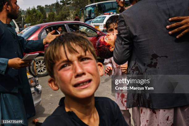 Man carries a bloodied child, as a woman lays wounded on the street after Taliban fighters use guns fire, whips, sticks and sharp objects to maintain...