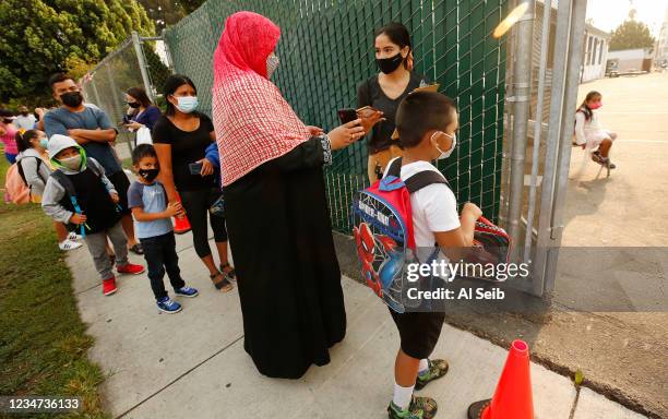 First Grader Ahnaf Abrar with his mother Shamima Abrar using the QR code on her phone checks in with Yazmin Magallon, Primary Promise Aide at...