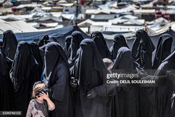 Women and a child queue to receive humanitarian aid packages at the Kurdish-run al-Hol camp, which holds relatives of suspected Islamic State group...