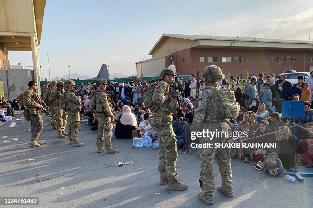 Soldiers stand guard as Afghan people wait to board a US military aircraft to leave Afghanistan, at the military airport in Kabul on August 19, 2021...