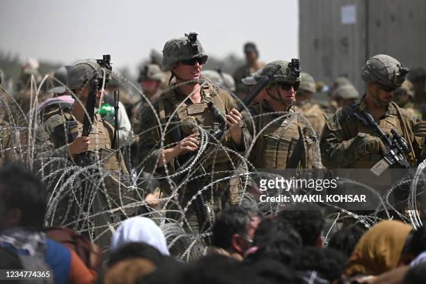 Soldiers stand guard behind barbed wire as Afghans sit on a roadside near the military part of the airport in Kabul on August 20 hoping to flee from...