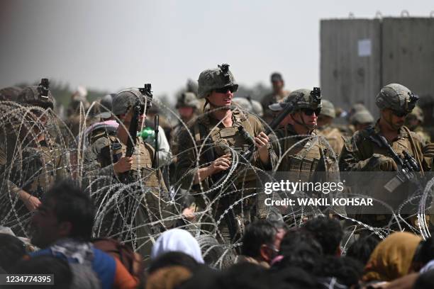 Soldiers stand guard behind barbed wire as Afghans sit on a roadside near the military part of the airport in Kabul on August 20 hoping to flee from...