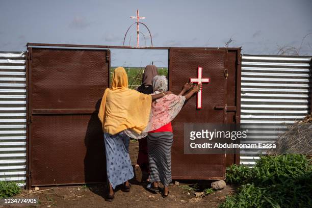 Three women touch a cross as they leave a Catholic church in Shagarab refugee camp on August 15, 2021 in Shagarab, Sudan. Situated about 70 km west...