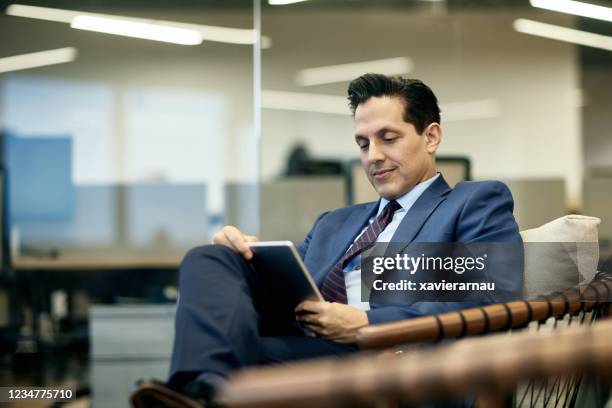 Hispanic Businessman Reading Digital Tablet in Armchair