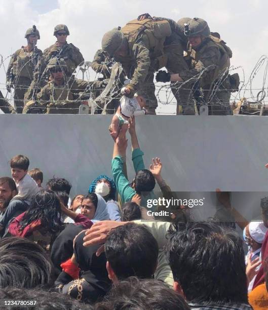 This image made available to AFP on August 20, 2021 by Human Rights Activist Omar Haidari, shows a US Marine grabbing an infant over a fence of...