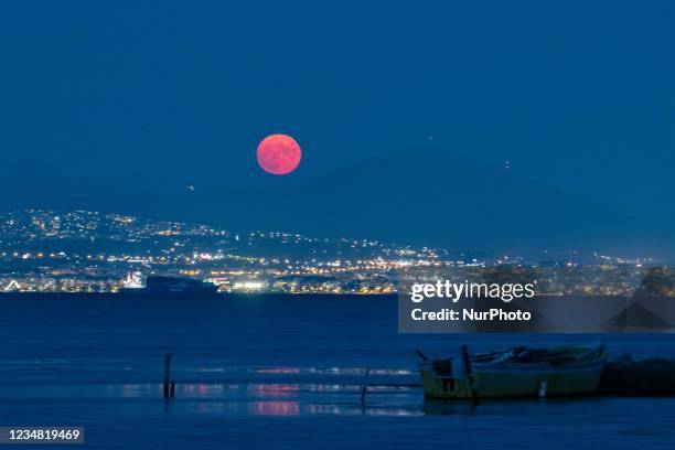 The moon with the city lights and local fishing boats. The August Sturgeon full moon rises behind the Hortiatis mountain and Thessaloniki city over...