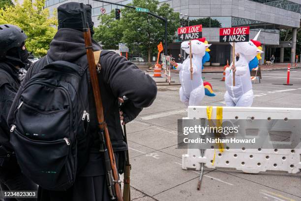 Counter protesters in unicorn costumes walk past an armed anti-fascist on August 22, 2021 in Portland, Oregon. Proud Boys and other far-right...
