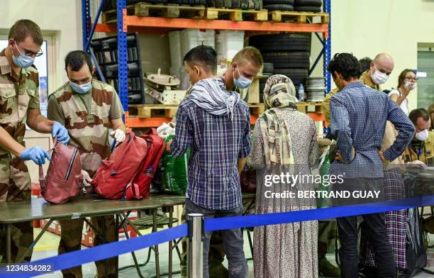 People have their luggages checked by soldiers in a reunion and evacuation center at the French military air base 104 of Al Dhafra, near Abu Dhabi,...