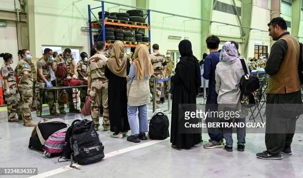 People wait to have their luggages checked by soldiers in a reunion and evacuation center at the French military air base 104 of Al Dhafra, near Abu...