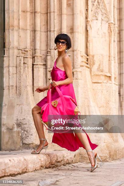 Model and artist Zoe Helali wearing a fuchsia colored Beatrice silk dress with open one shoulder, loose silhouette and asymmetric hem by Sasha La...