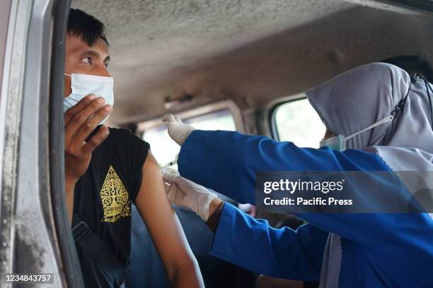Health worker inoculates a resident with covid vaccine inside a car. A number of Makassar City residents received vaccine at drive-thru vaccine...