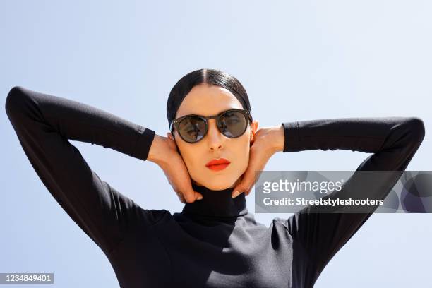 Model and artist Zoe Helali wearing a black midi length longsleeve turtleneck dress with thigh high slit by Wolford and sunglasses by & Other Stories...