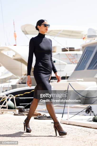 Model and artist Zoe Helali wearing a black midi length longsleeve turtleneck dress with thigh high slit by Wolford, black thigh high stay-up...