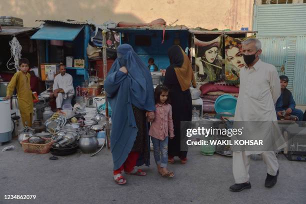 Burqa clad Afghan woman looks for items to buy at a shop displaying used household items for sale at a market area in Kabul on August 25 which were...