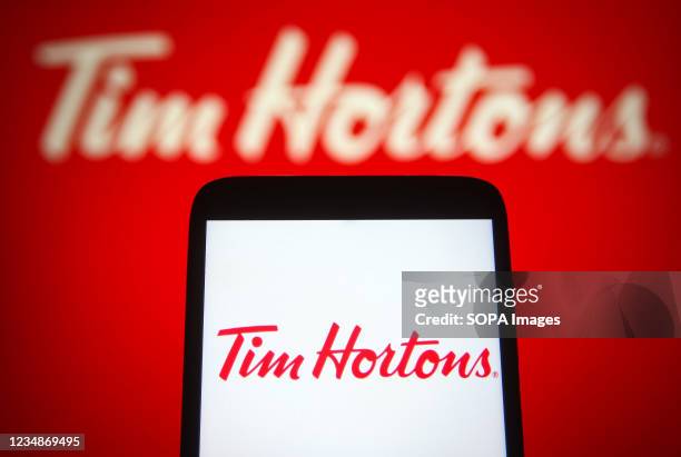In this photo illustration a Tim Hortons logo of a multinational fast food restaurant chain is seen on a smartphone and a pc screen.