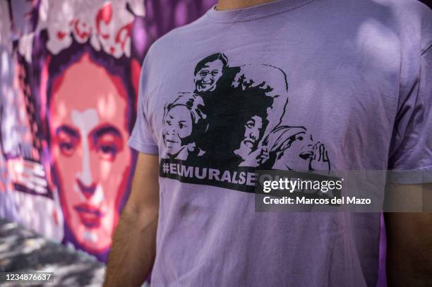 Man wearing a shirt with the slogan 'the mural stays' stands next to a feminist mural that is being repainted by members of UNLOGIC artistic group....