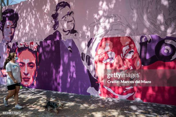 Woman passing by a feminist mural that is being repainted by members of UNLOGIC artistic group. The mural appeared vandalized during the past...