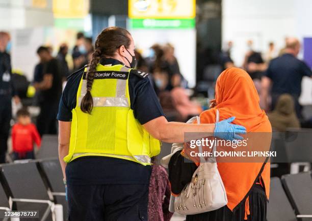 Member of Border Force staff assists an Afghan refugee on her arrival on an evacuation flight from Afghanistan, at Heathrow Airport, London on August...