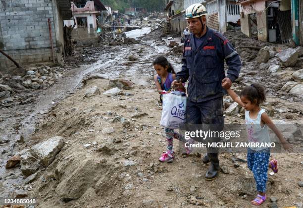 Firefighter walks with two girls in an area where several homes were destroyed by a mudslide caused by heavy rains in Valle del Mocoties community,...