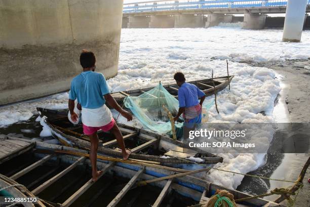 Fisherman seen at work in the heavily polluted waters of Yamuna River with a thick white layer of toxic foam showing high water pollution levels.