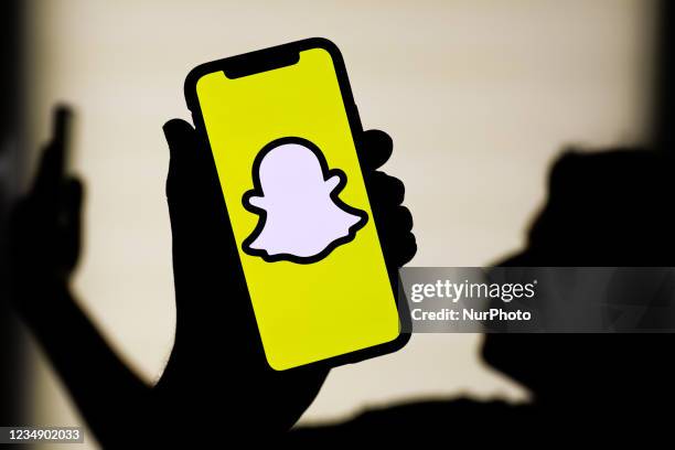 Snapchat logo displayed on a phone screen and silhouette of a woman with a phone in the background are seen in this illustration photo taken in...