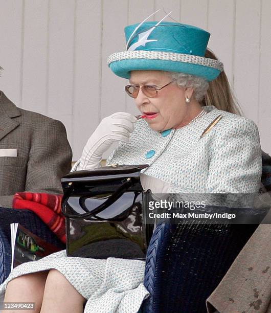 Queen Elizabeth II applies her lipstick as she attends the annual Braemar Gathering and Highland Games at The Princess Royal and Duke of Fife...