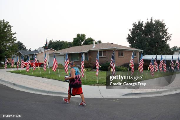 Neighbor walks by American flags and yellow ribbons that line the sidewalk outside the house of Darren Hoover, whose son, Staff Sgt. Taylor Hoover...