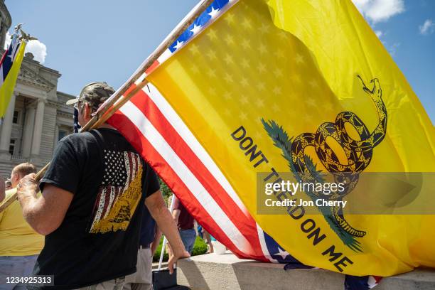 Man with a Gadsden flag, a US flag, and a Confederate battle flag listens to a speaker during the Kentucky Freedom Rally at the capitol building on...