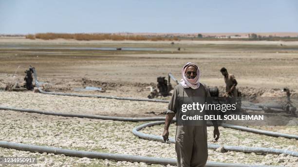 Man walks near water pumps drawing water from the Lake Assad reservoir, in the village of al-Tuwayhinah near the Tabqa Dam along the Euphrates river...