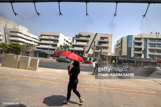 Woman walks with a parasol umbrella underneath sprinklers releasing water vapour along a street to relieve pedestrians amidst a heatwave in Dubai on...