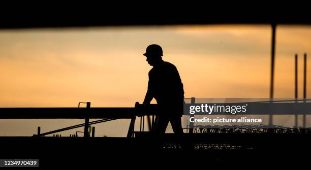 Dpatop - 31 August 2021, Lower Saxony, Hanover: The silhouette of a construction worker stands out against the discoloured morning sky at a building...